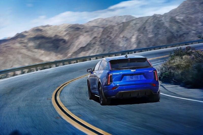 Rear View of a Blue 2026 OPTIQ-V Driving on a Curve of a Mountain Row | Earnhardt Cadillac in Scottsdale AZ